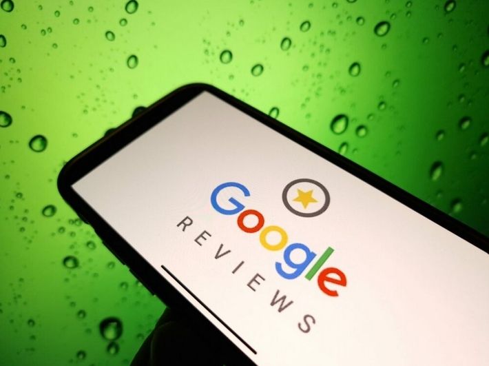 Smartphone mit der geöffneten Webseite von Google Reviews vor grünem Hintergrund mit Wassertropfen